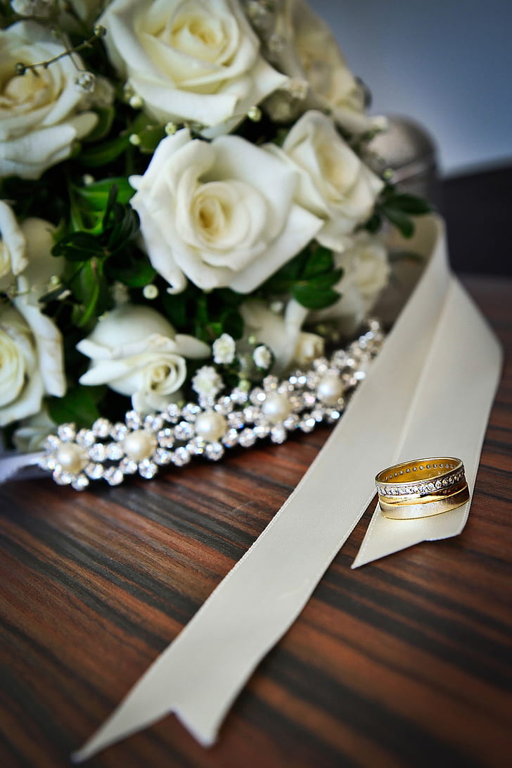 gold-colored clear gemstone encrusted ring on white ribbon near bouquet of white roses
