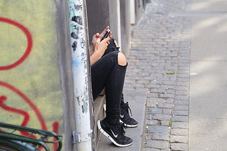 shallow focus photography of person wearing distressed black jeans using smartphone