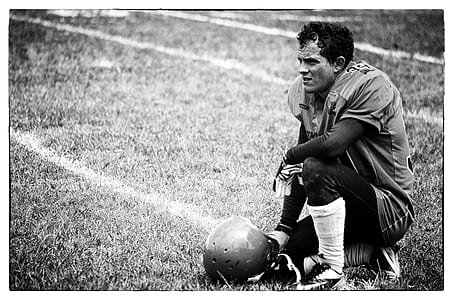 grayscale photo of football player kneeling on grass