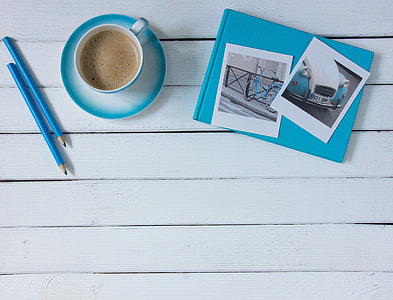 two blue pencils, blue-and-white teacup and saucer set, and blue and white photo album with photos on top