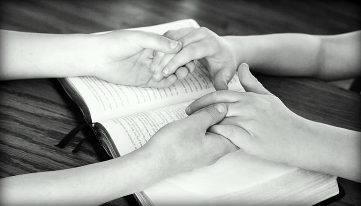 grayscale photography of two person holding hands on book