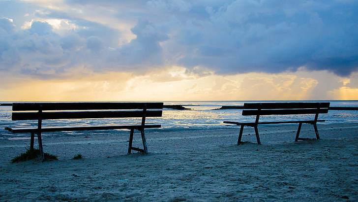 two silhouette benches near seashore at daytime