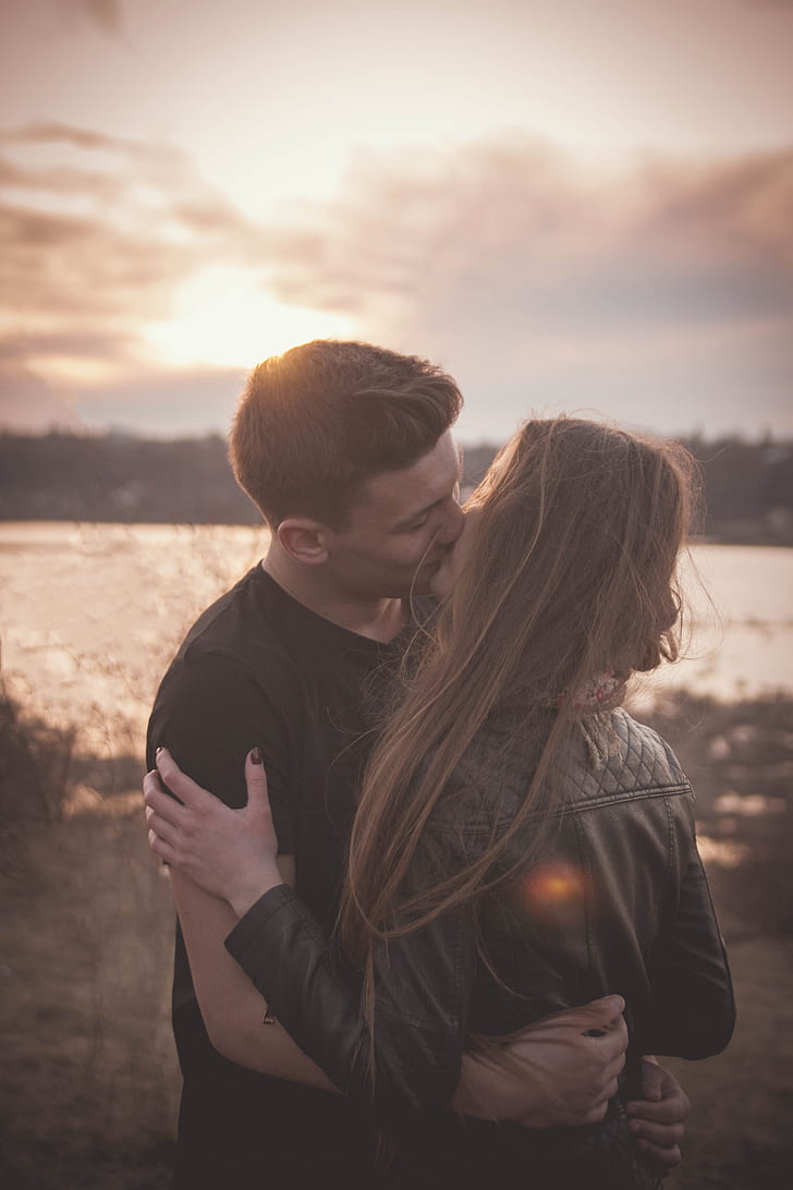 man kissing woman near body of water during sunset