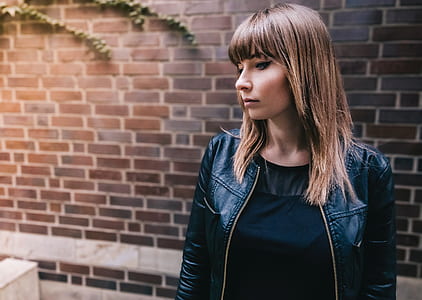woman in black leather jacket standing near brown brick wall