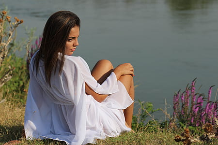 Woman Wearing White Sitting on Green Grass Near Body of Water