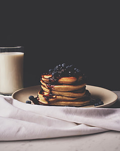 food photography of pancake top with blueberries on white ceramic plate beside a glass of milk