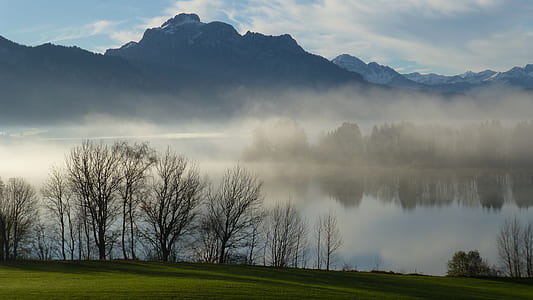 body of water covered with fog near mountain range