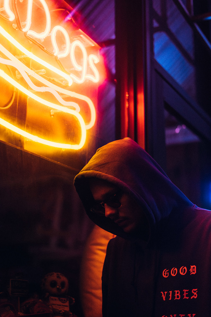 man wearing hoodie standing near neon signage