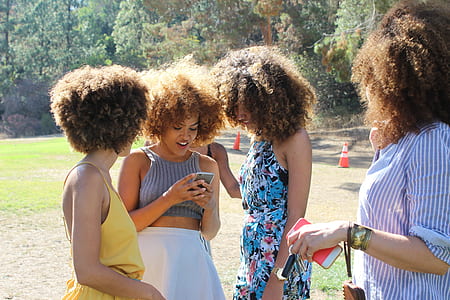four women with brown afro hairs standing in grass field at daytime