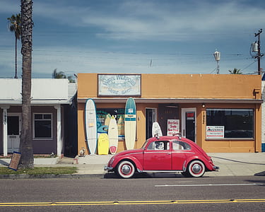 red Volkswagen Beetle on road near store at daytime