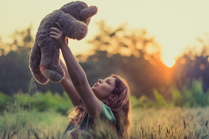 woman in green shirt holding brown teddy bear during sunrise