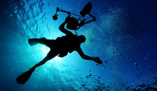 person wearing diving suit holding camera underwater during day