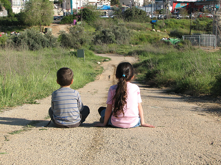 two girl and boy sitting on brown road
