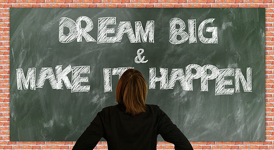 person in black long-sleeved shirt standing front of Dream Big & Make It Happen text