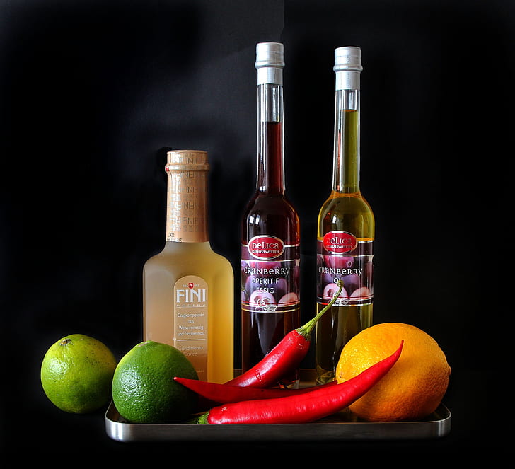 two chili peppers and limes near glass bottles