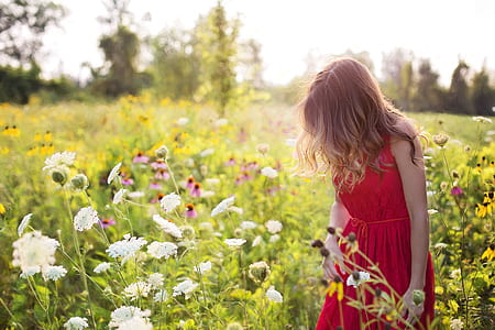 woman in red sleeveless dress standing beside flower field at daytime
