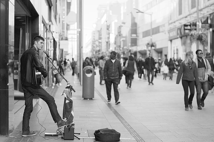grayscale photo of man performing instrument at street