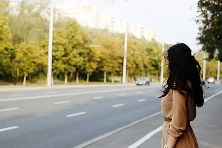 woman in brown long-sleeved dress standing in front of asphalt road during daytime