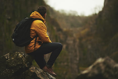 man with yellow hoodie sitting on rock boulder