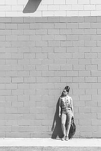 grayscale photo of a woman leaning back on a concrete wall