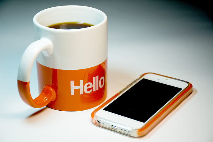 white iPhone 5 with orange case near white and orange hello ceramic coffee mug