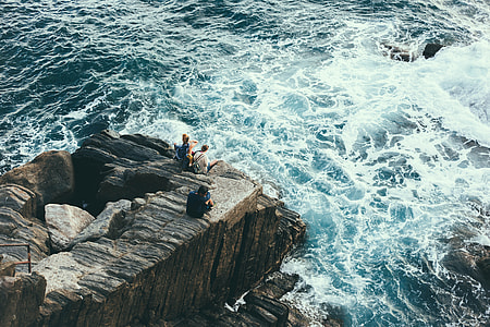 two men and woman on rock cliff beside a sea
