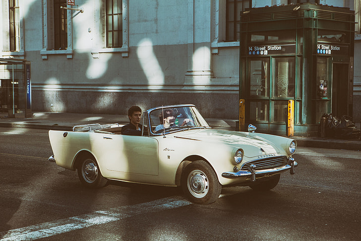 Two people sit in an open-top classic car (Sunbeam Alpine) on the streets of Manhattan, New York City