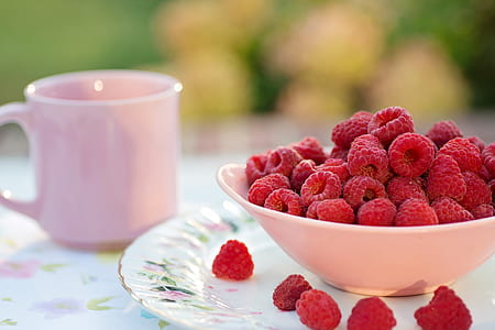 raspberries in white ceramic bowl near ceramic mug in selective focus photography at daytime