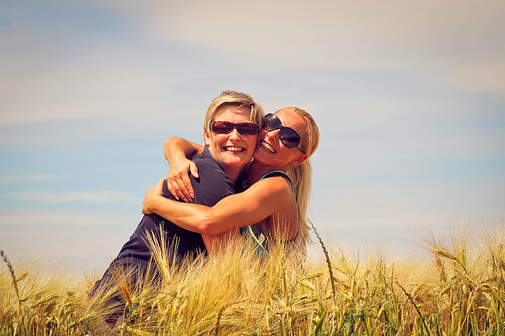 two women hugging beside brown grasses during daytime