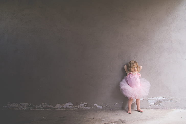 toddler's wearing pink tutu dress leaning on wall