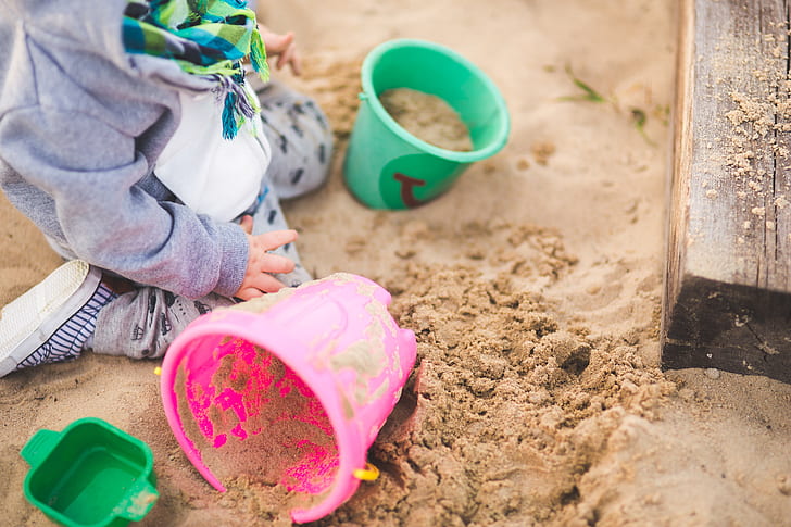 toddler's playing sand on green and pink buckets