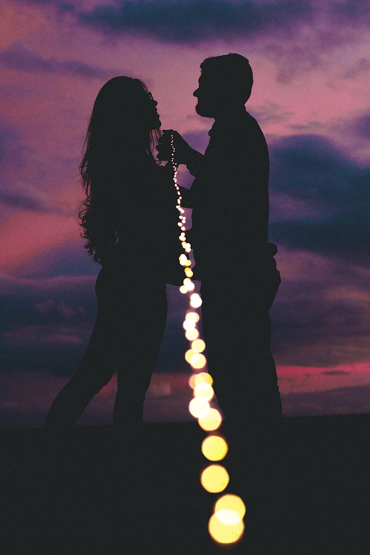 silhouette of woman and man holding string light during nighttime