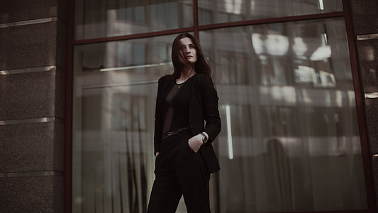 woman in black blazer and black pants standing near glass window