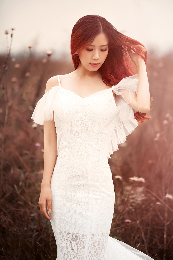woman in white cold-shoulder dress standing in forest while holding her hair