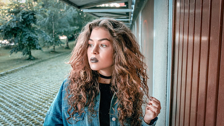 woman wearing blue denim jacket holding her curly hair