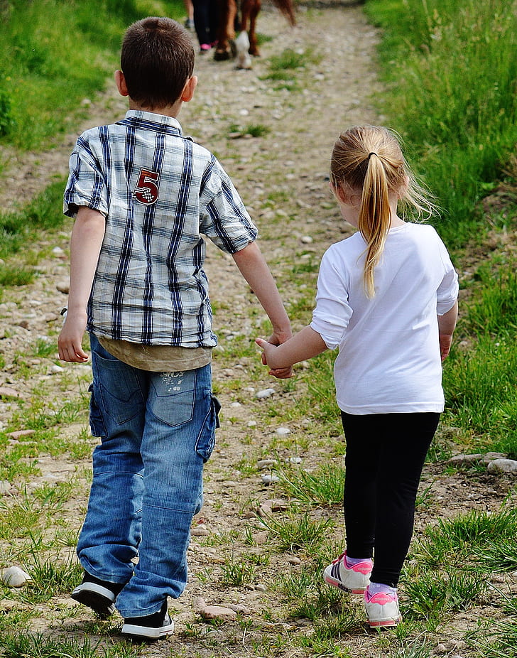 boy and girl holding hands walking on brown pathway
