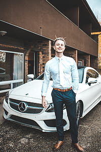 man wearing teal dress shirt, white necktie and green pants standing near white Mercedes-Benz coupe