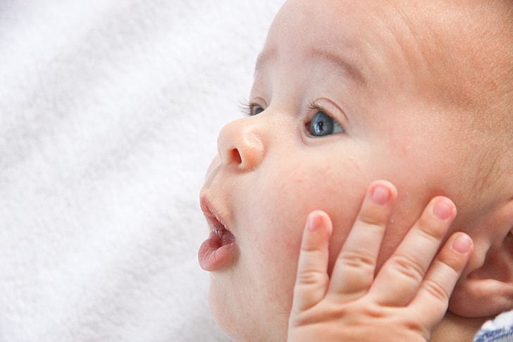 closeup photo of baby holding his face