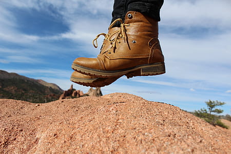 person wearing brown leather cap-toe chunky heel combat boots jumping over brown soil