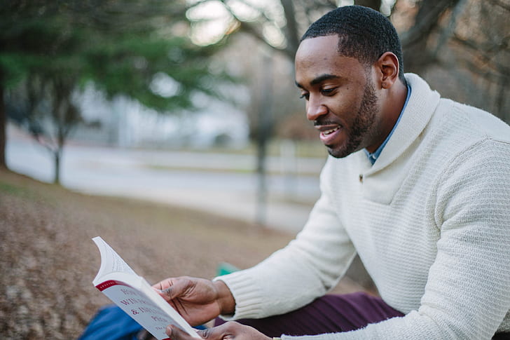 man wears white sweater and reading a book