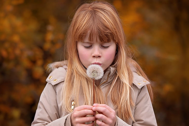 girl in brown coat about to blow dandelion