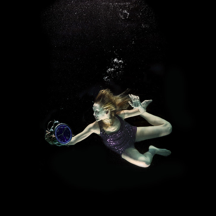 underwater photography of woman holding round alarm clock
