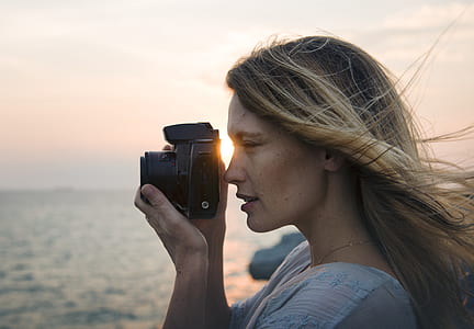 portrait photography of woman holding black DSLR camera near body of water during daytime