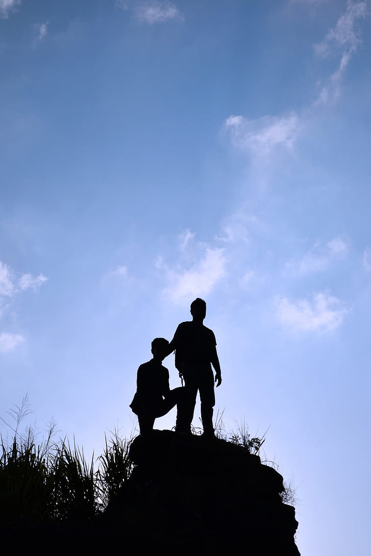 silhouette photo of two boy standing on heels under blue sky