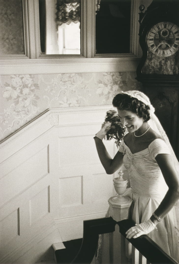grayscale photo of woman in wedding gown standing beside stair railing