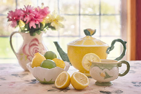 yellow ceramic teapot with lemonade with cup beside bowl and flower centerpiece