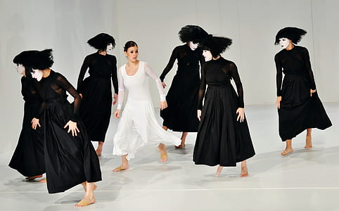 woman wearing white scoop-neck long-sleeved dress and group of woman wearing black long-sleeved dresses standing on white floor