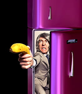 man wearing gray suit jacket holding banana in purple top-mount refrigerator