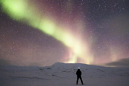 man standing on middle of snow-covered field with Aurora Borealis in background