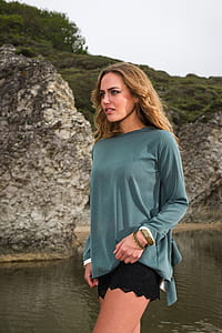woman in green long-sleeved shirt and black shorts near body of water